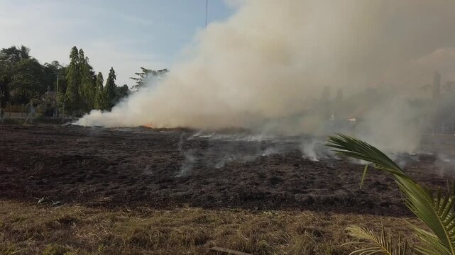 Grass on a soccer field burning in flames. The scene shows fire spreading across dry grass in an outdoor sports area, creating smoke and visible fire damage.