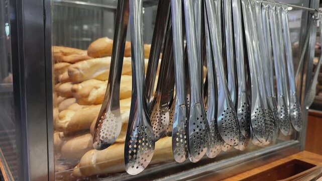 Close up of Row of Bakery Tongs With Baguettes in Background in self-service supermarket 