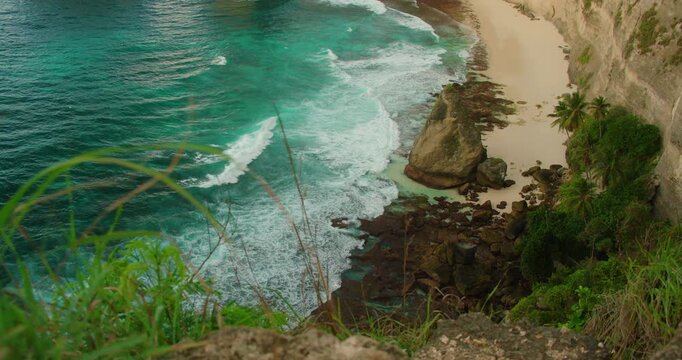 White ocean waves roll onto the rocky shore of Diamond Beach as seen from a high cliff viewpoint in Nusa Penida Bali
