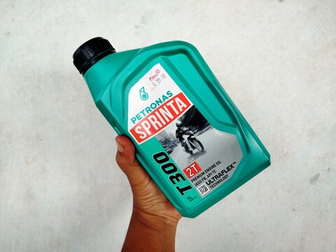 KUALA TERENGGANU, MALAYSIA- AUGUST 28. 2026: Close-up of a hand holding a green container of Petronas Sprinta T300 2T motorcycle engine oil with Ultraflex technology over concrete floor.