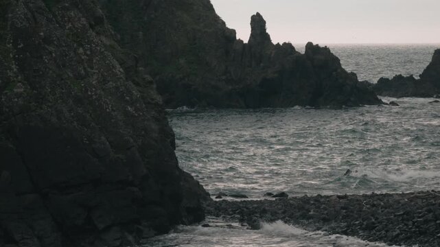 Waves crashing onto a beach beneath steep coastal cliffs