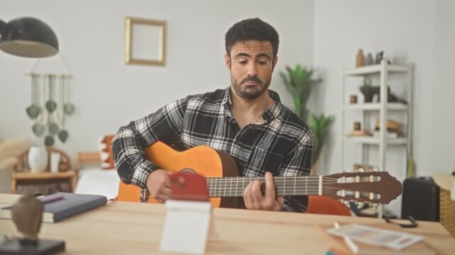 Man plays classical guitar with hands on fretboard and strumming while recording on a smartphone in a studio; concentration practice.