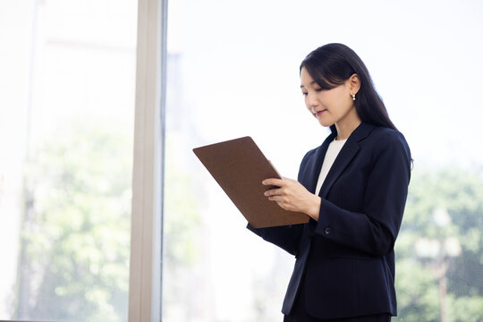 Young Japanese businesswoman taking notes on a clipboard by a bright window