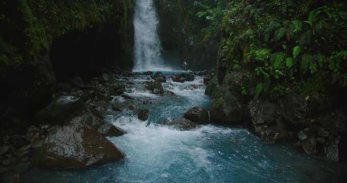 Narrow gorge with waterfall plunging into blue water surrounded by dark rocks in the jungle forest