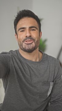 Man on bed smiling and waving at camera inside a building, leaning toward lens with visible hand gesture; friendly connection.
