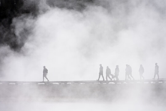 Tourists walking on boardwalk in early morning steam at Midway Geyser Basin exploring geothermal features, summer vacation at Yellowstone National Park
