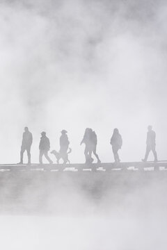 Tourists walking on boardwalk in early morning steam at Midway Geyser Basin exploring geothermal features, summer vacation at Yellowstone National Park
