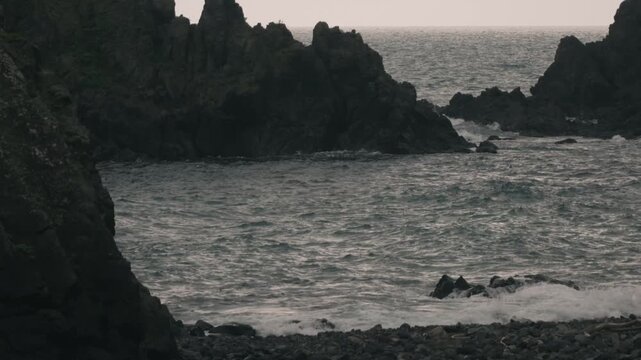 Waves crashing onto a beach beneath steep coastal cliffs