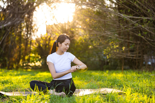 Woman sitting on a yoga mat looking down at her smartwatch in a sunny park