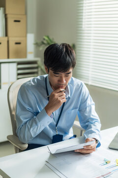 Office worker holding pen and checking report document thoughtfully at desk.