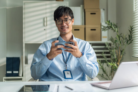 Office worker wearing glasses smiling confidently while holding smartphone at desk.
