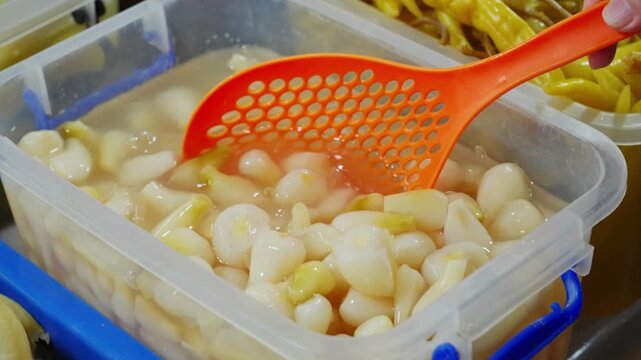 Food close-up of pickled garlic cloves being scooped out with a slotted spoon