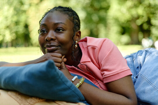 Young adult African American woman lying on grass in park during outdoor psychotherapy session, looking away thoughtfully. Image suitable for mental health and outdoor counseling campaigns