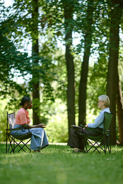 Young African American woman talking to senior Caucasian female therapist in park, representing outdoor psychotherapy. Image suitable for mental health and wellness campaigns, vertical