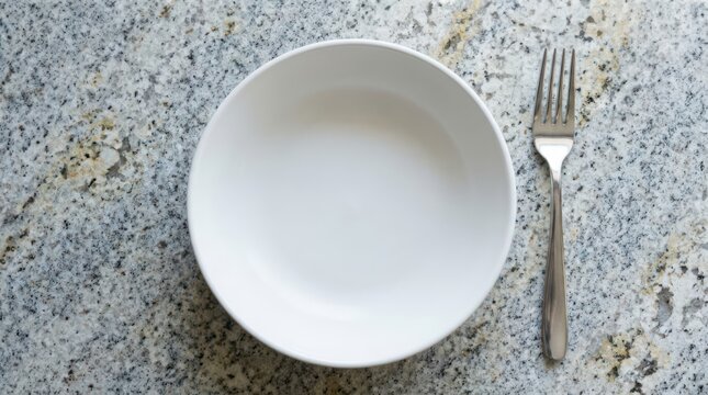 Empty white bowl and a silver fork placed on a textured grey granite countertop
