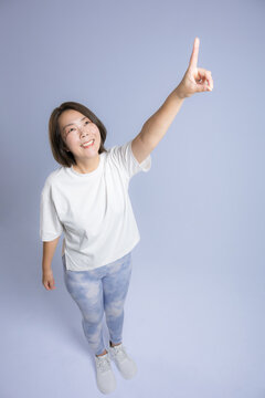 [ブルー背景]笑顔で指差す腕を高く伸ばして運動する女性、ダイエット成功や健康的で前向きな40代のミドル世代のフィットネスイメージ