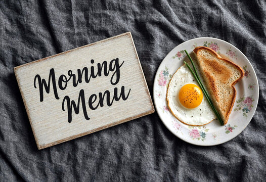 Delicious breakfast plate with fried egg toast and green onion on tablecloth next to morning menu sign