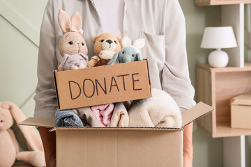 Fototapeta premium Charity donation and community support, person holding cardboard box with toys and clothes for humanitarian aid and social responsibility in home interior