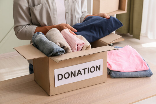 Donation and charity work, person packing clothes into a cardboard box for humanitarian aid and community support in a home environment