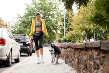 Active lifestyle and pet ownership, woman walking with her husky dog on a city sidewalk during a morning exercise routine in an urban neighborhood © Pixel-Shot