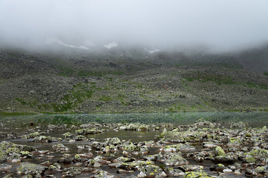 Rocky lake shore with mountain range and fog