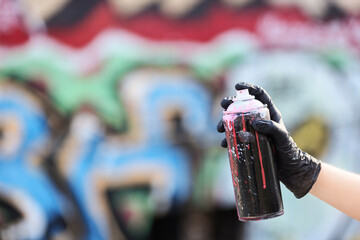 Street art and urban creativity, person holding a spray paint can with black gloves in front of a colorful graffiti wall for artistic expression © Pixel-Shot