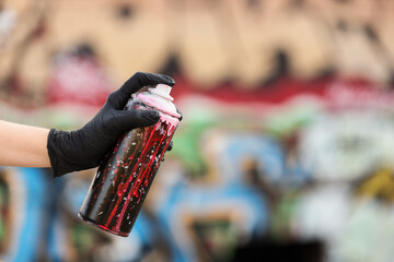 Street art and urban creativity, artist hand in black glove holding a spray paint can with dripping red and white colors against a graffiti wall © Pixel-Shot