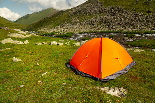 Bright orange camping tent pitched on green grassy meadow