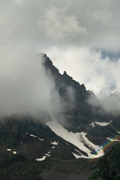 Dramatic mountain peak obscured by clouds with snow and rainbow