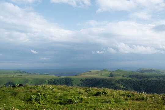 Green rolling hills and mountains under cloudy sky