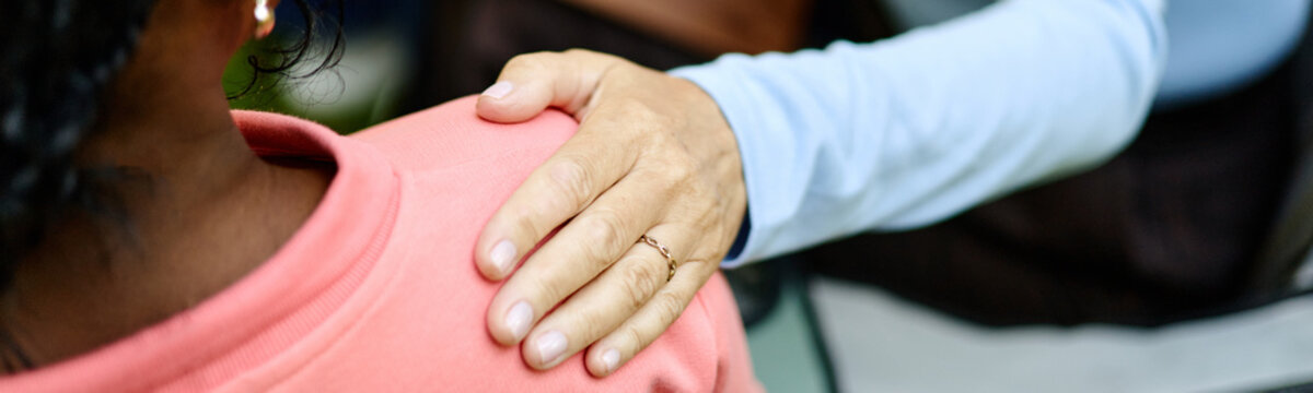 Close up header of Caucasian therapist hand resting on shoulder of Black female patient during outdoor psychotherapy session, representing mental health support and counseling services