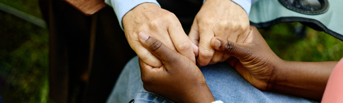 Close up header of African American therapist holding hands of senior Caucasian woman during outdoor psychotherapy session, representing mental health support and empathy