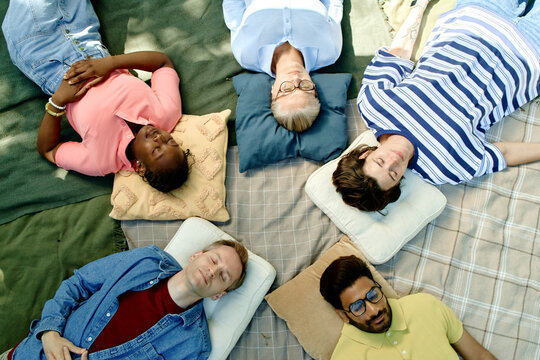 Diverse group of multiethnic adults lying in circle on blankets in park during outdoor psychotherapy session. High angle shot representing mental health support and group therapy