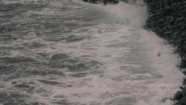 Waves crashing violently against numerous rounded stones along a rocky shore
