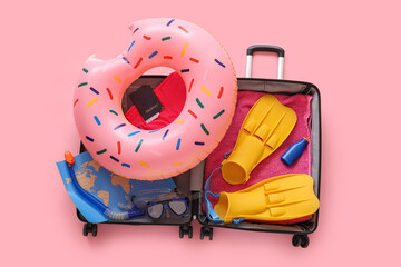 Summer vacation planning and travel preparation, open suitcase with beach accessories and swimming gear on a pink background for holiday trip © Pixel-Shot