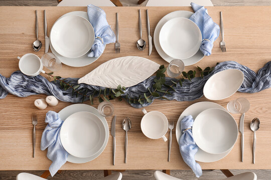 Table setting for dinner party, elegant dining arrangement with blue napkins and eucalyptus on wooden table for festive celebration and home hosting