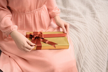 Naklejka premium Gift giving and celebration woman holding a gold wrapped present with a red ribbon for holidays birthday anniversary or special occasion surprise