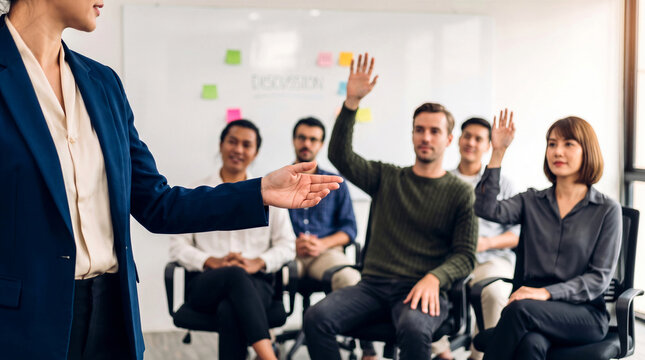 Businesswoman leading a corporate training seminar while diverse audience members raise hands to ask questions 