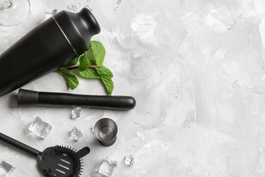 Different bartender utensils with mint leaves and ice cubes on light grunge background