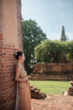 One Asian teenage girl dressed in traditional Thai outfit standing at old town brick wall, holiday travel in Ayutthaya historical park, Southeast Asia, ancient ruins heritage,  tourist destination.