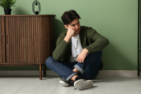Depressed young man sitting on floor at home