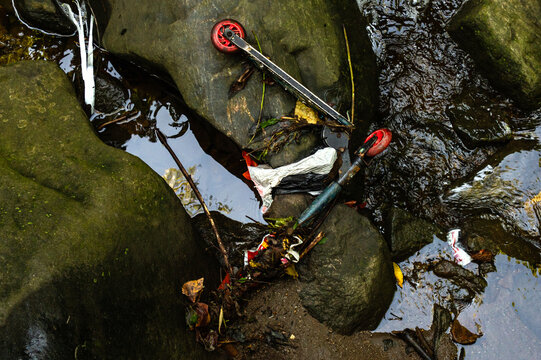 An abandoned kid's scooter on a stream covered in garbage 
