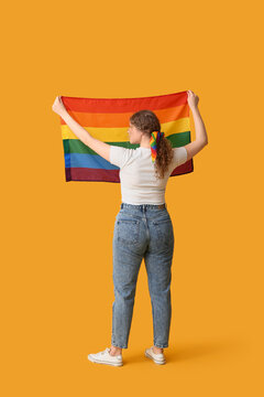 Young woman with LGBT flag and hairscarf on yellow background, back view