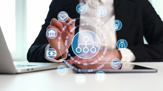 A person in a business suit is using a digital tablet while sitting at a desk. Various technology icons surround the device. This scene takes place in an office setting during the day.