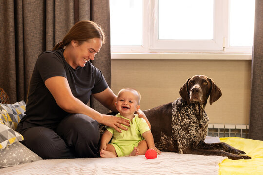 Mother Supports Laughing Baby Beside German Shorthaired Pointer