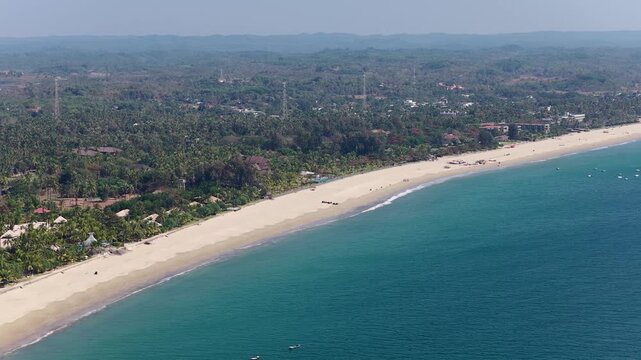 Aerial drone view of golden sand beach, palm trees, hotels and waves and coast of Andaman Sea in Asia. Aerial panorama of coast of famous resort village Ngwe Saung in Myanmar.