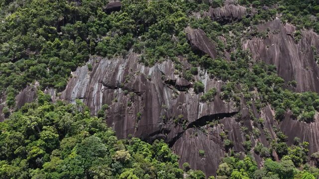 Aerial Drone Pullback and Rise from a Majestic Rock Formation on Yang Hanh Mountain, Dak Lak, Vietnam, Revealing Dramatic Patches of Sunlight and Clouds Moving Across the Rugged Stone