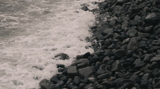 Waves crashing violently against numerous rounded stones along a rocky shore
