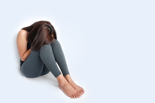 A sad and depressed woman sitting alone on the floor with her head down, representing mental health issues, sadness, emotional pain, loneliness, and psychological distress.on isolated white background