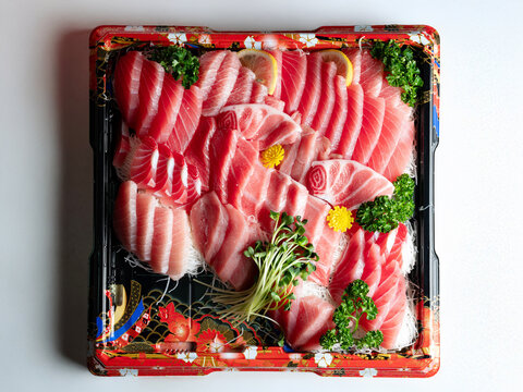 Premium assorted tuna sashimi platter including otoro and chutoro in a takeout bento box, white background with copy space